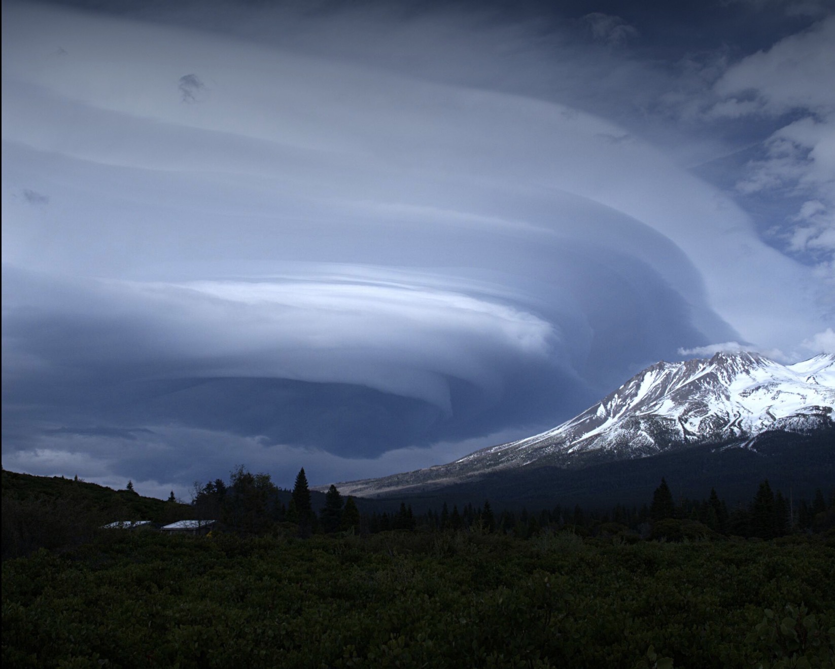 Dramatic lenticular cloud spiraling above a snow-capped Mount Shasta at dusk